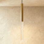 Clérachic gold tube pendant with the longest bubble acrylic shade, glowing warm against a limewash wall.