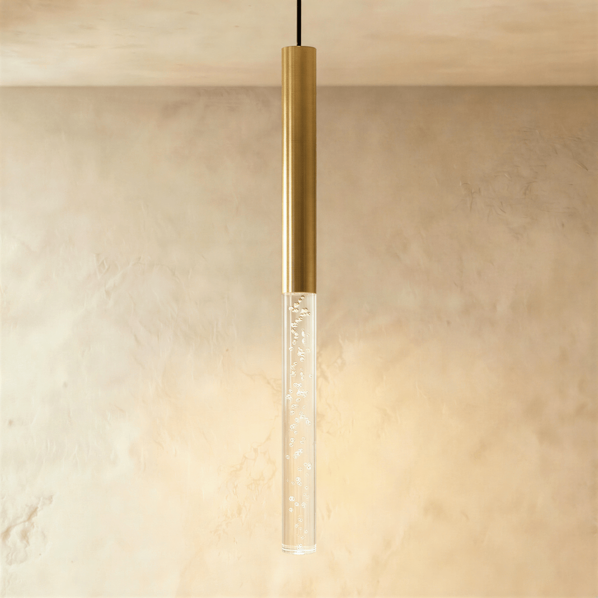 Clérachic gold tube pendant with the longest bubble acrylic shade, glowing warm against a limewash wall.