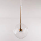 The Clérachic Bubble Cluster Pendant Light in its single clear-glass globe version, hanging on a slim brushed-brass rod.