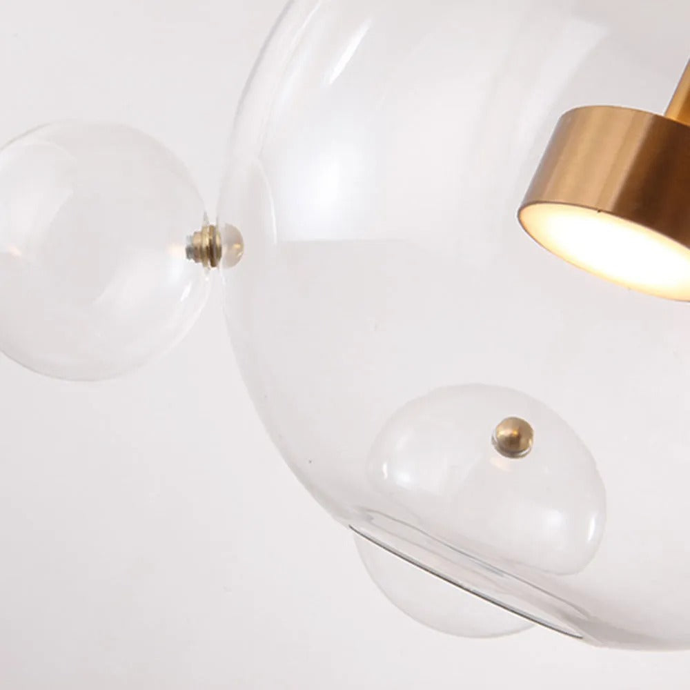 Close-up of the Clérachic Bubble Cluster Pendant Light's glowing brass LED module beside one of its clear-glass satellite bubbles.