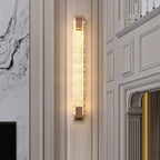 Tall narrow Clérachic wall light glowing in a hallway with white wall panelling, a marble wall and an arched opening.