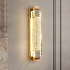 Close-up of the lit bubble-crystal panel and gold end caps of this Clérachic wall light on a soft grey wall.