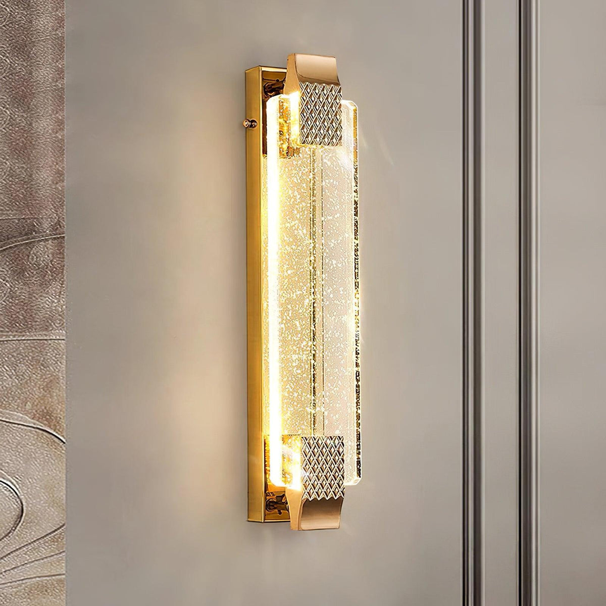 Close-up of the lit bubble-crystal panel and gold end caps of this Clérachic wall light on a soft grey wall.