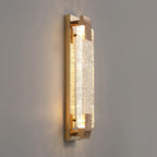 Rose gold wall light from Clérachic photographed from the side, the textured end caps and crystal bar glowing on grey.