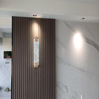 Clérachic crystal wall light mounted on a dark fluted panel next to a white marble wall and ceiling downlights.
