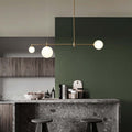 A Clérachic 3-head bubble-glass bar pendant lights a kitchen island with terrazzo counter, dark green wall and a bowl of nuts below.
