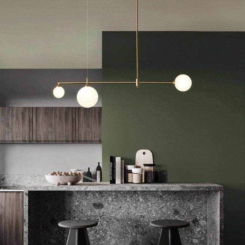 A Clérachic 3-head bubble-glass bar pendant lights a kitchen island with terrazzo counter, dark green wall and a bowl of nuts below.