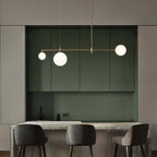 This Clérachic bubble-glass bar pendant with three opal globes hangs over a marble counter lined with grey upholstered stools.