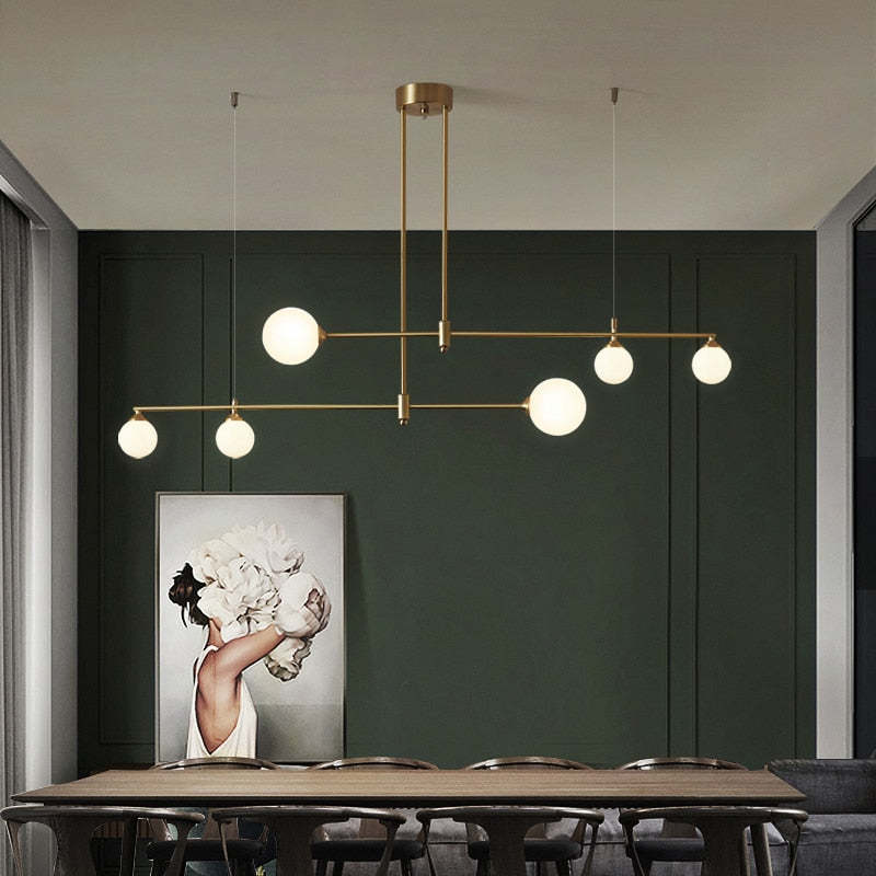 The Clérachic 6-head bubble-glass bar pendant spans a dining table set below a green panelled wall and a framed floral artwork.