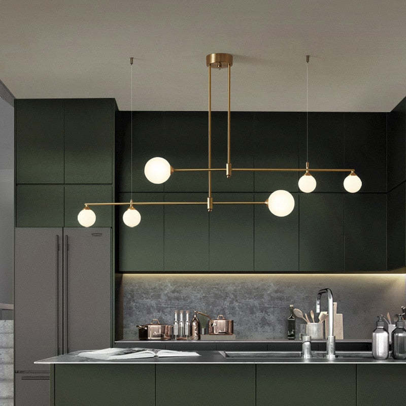 A Clérachic 6-head bubble-glass bar pendant in brass-tone metal lights a dark green kitchen with under-cabinet lighting by the sink.