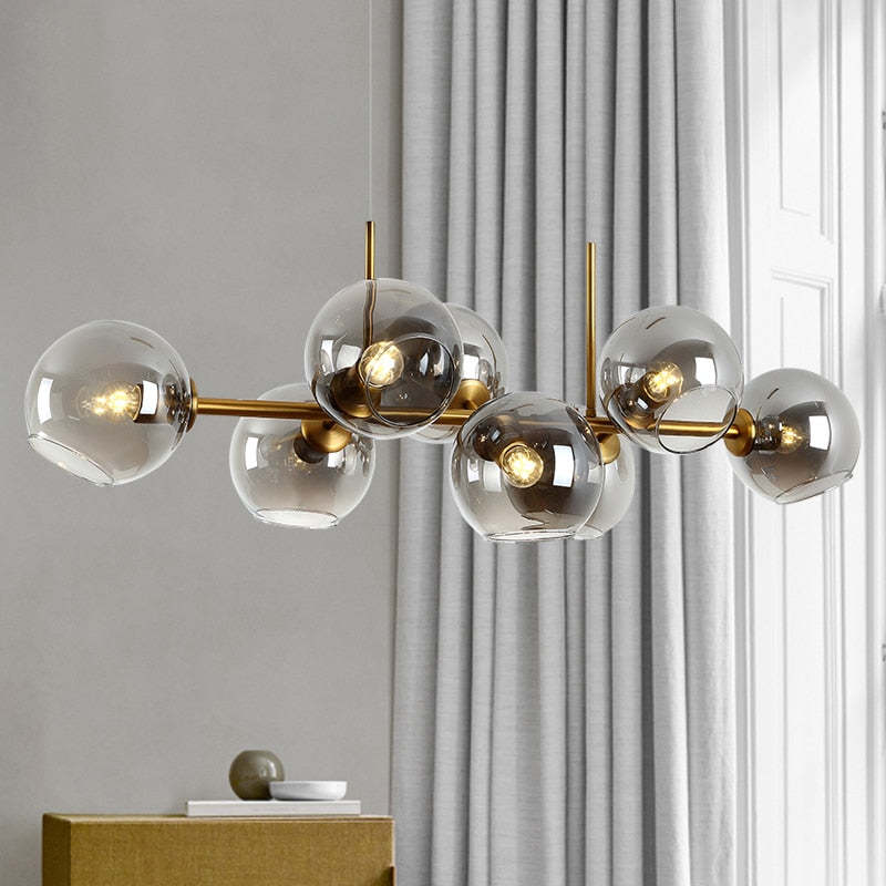 Gold Clérachic bubble glass pendant with smoke gray glass globes, glowing against a soft curtain backdrop.