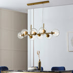 Gold Clérachic bubble glass pendant light glowing above a dark marble kitchen island with blue velvet chairs.