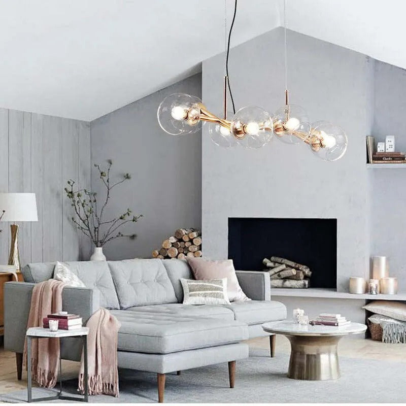 Gold Clérachic bubble glass pendant light hanging above a gray sofa and fireplace in a vaulted living room.