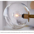 Close-up of a single clear glass globe and its filament bulb on the gold Clérachic bubble glass pendant.