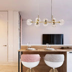 Gold Clérachic bubble glass linear pendant light above a breakfast bar with cushioned stools and place settings.