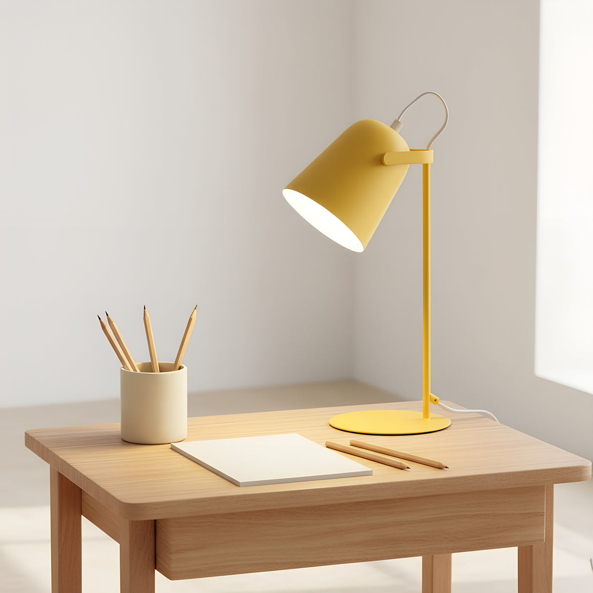 The yellow desk lamp on a pale wood study desk in daylight, shade tilted over a blank pad with pencils beside it