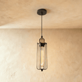 Clérachic slim black wire-cage pendant with a brass socket and a long amber filament bulb, hung from a black canopy.