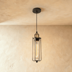 Clérachic slim black wire-cage pendant with a brass socket and a long amber filament bulb, hung from a black canopy.
