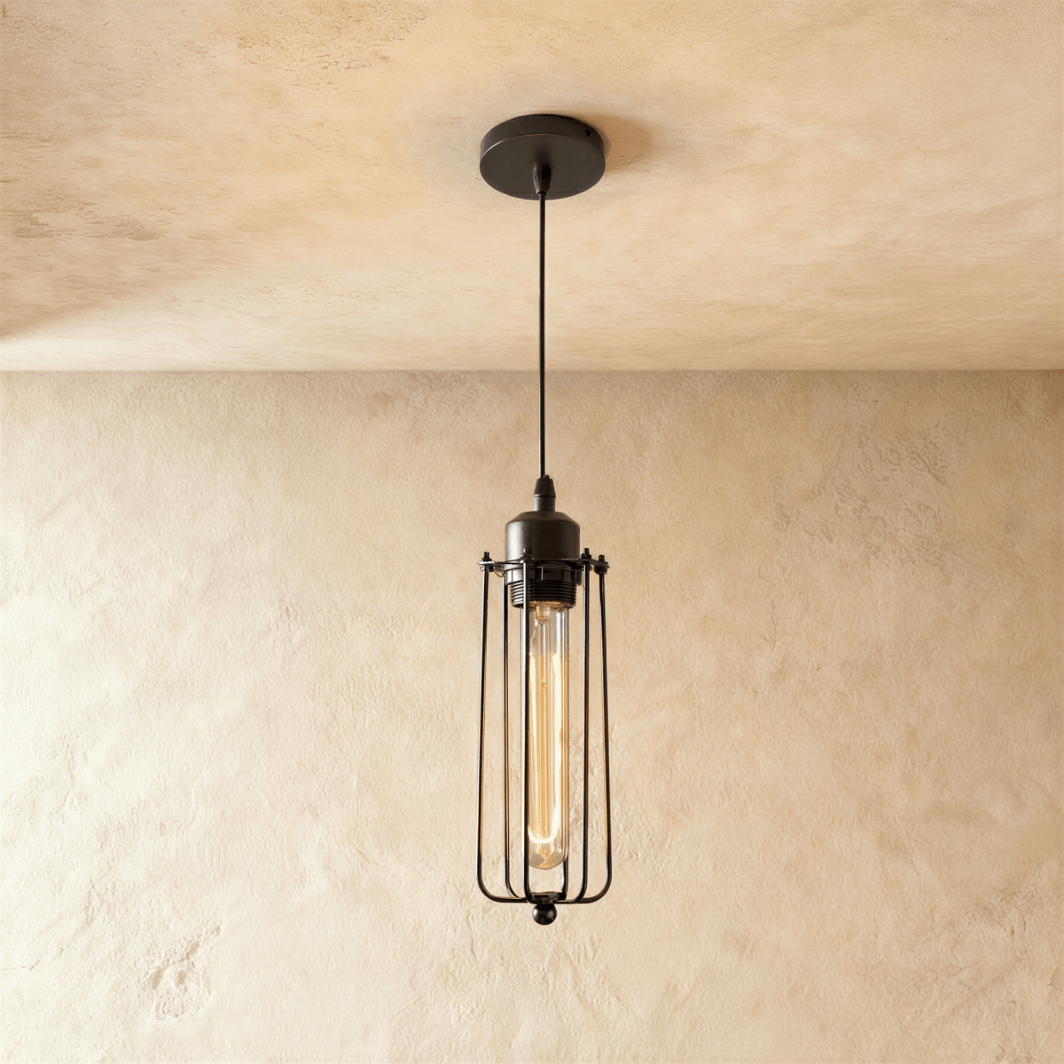 Clérachic slim all-black wire-cage pendant with a long filament bulb glowing amber, on a black cord and canopy.