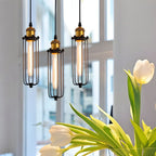Clérachic three slim black cage pendants with brass sockets and glowing tube bulbs, by a bright window with white tulips.