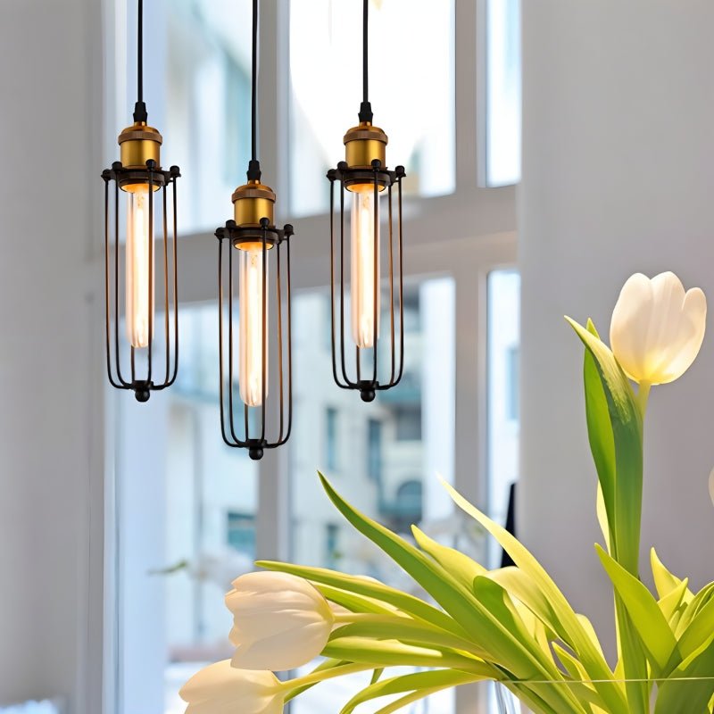 Clérachic three slim black cage pendants with brass sockets and glowing tube bulbs, by a bright window with white tulips.