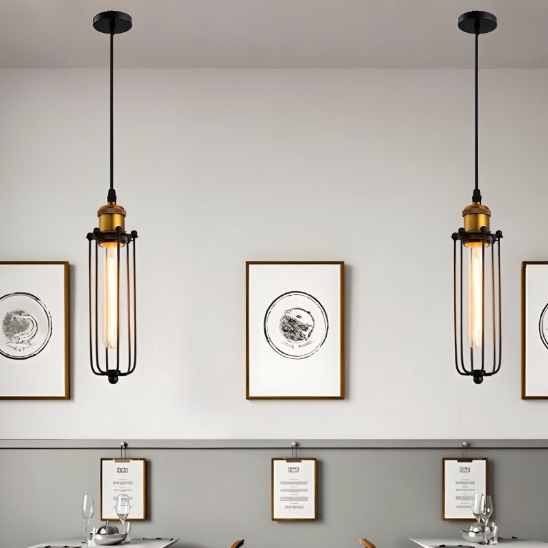 Clérachic two slim black cage pendants with brass sockets and tube bulbs, hung on a pale wall above a dining area.