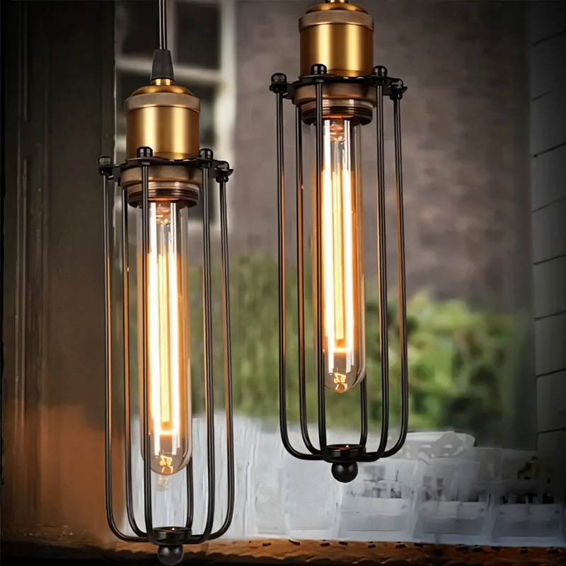 Clérachic close-up of two black wire-cage pendants, brass sockets above long glowing tube filament bulbs.