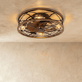 Clérachic flush ceiling fan with a light: a round caged bronze frame with wood-look rim, fan blades and warm filament bulbs in the studio.