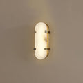Clérachic Calla wall light lit on a taupe wall, oval alabaster panel held by two brass straps.