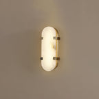 Clérachic Calla wall light lit on a taupe wall, oval alabaster panel held by two brass straps.