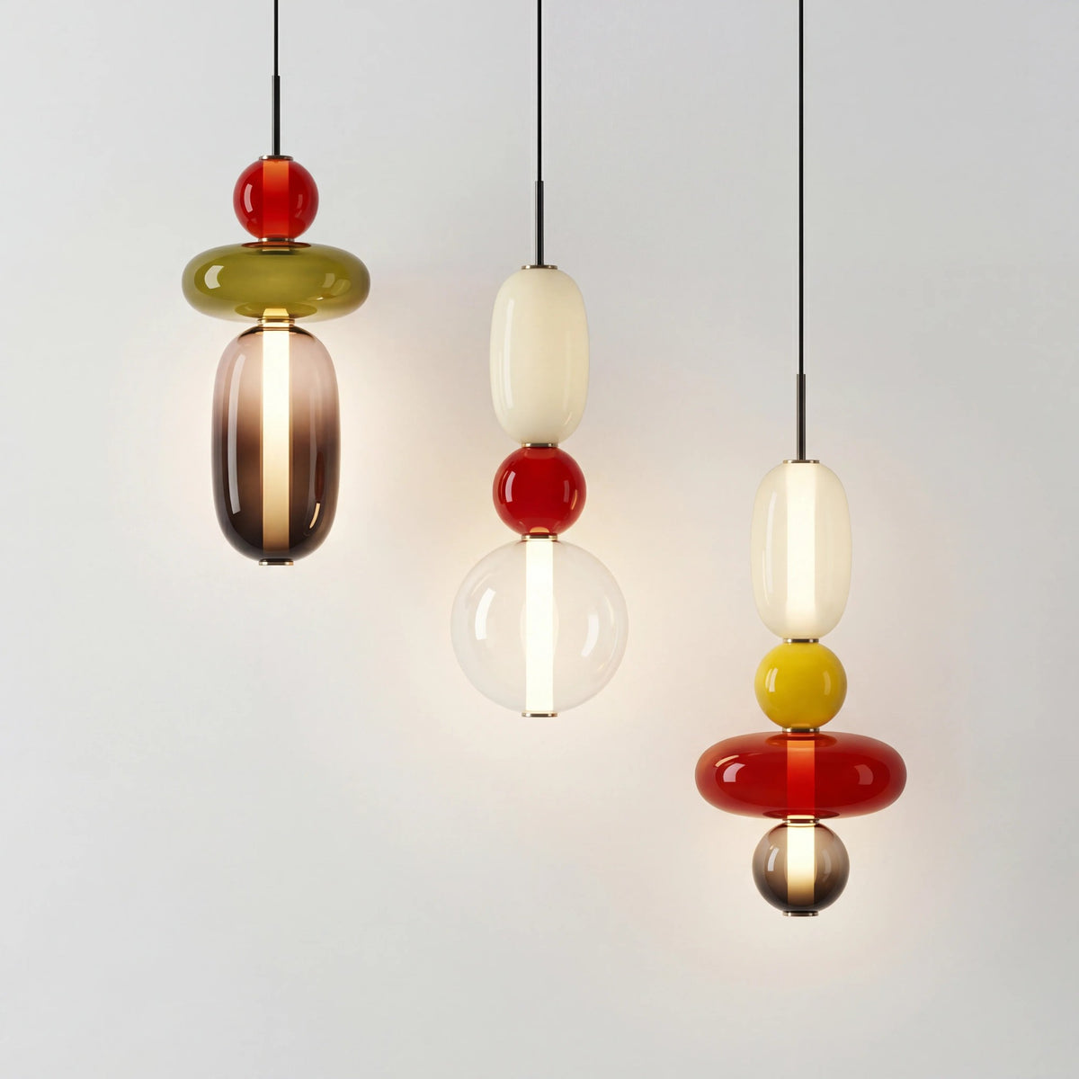 Three Clérachic pendants lit side by side on a pale wall, one stacking a red ball and olive disc over a smoked glass capsule.