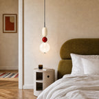 Clérachic pendant with a red glass ball between an opal capsule and a globe, hung beside an olive velvet headboard.