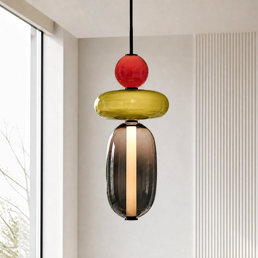 Close view of a Clérachic pendant lit from within, a red ball and olive disc stacked above a smoked glass capsule.