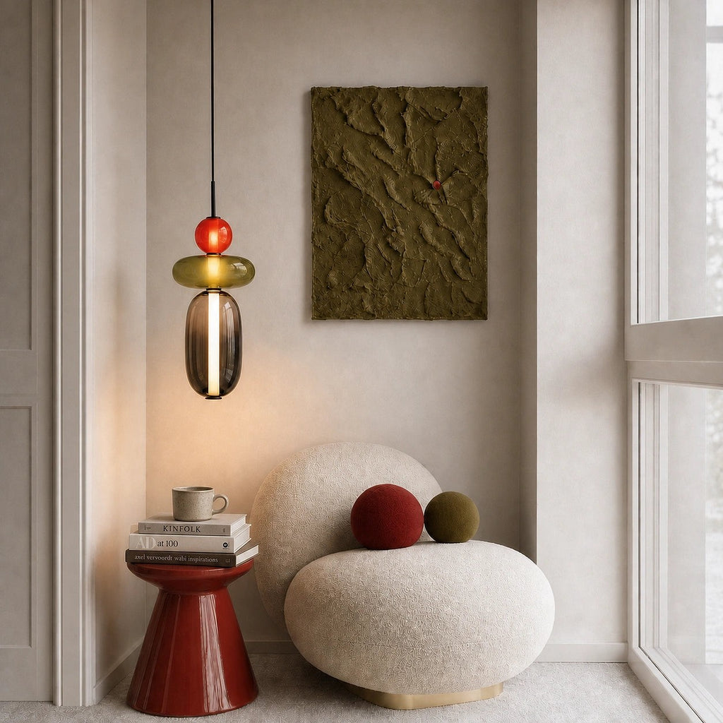 Clérachic pendant hanging in a quiet reading corner above a round boucle chair, its red ball and olive disc softly lit.