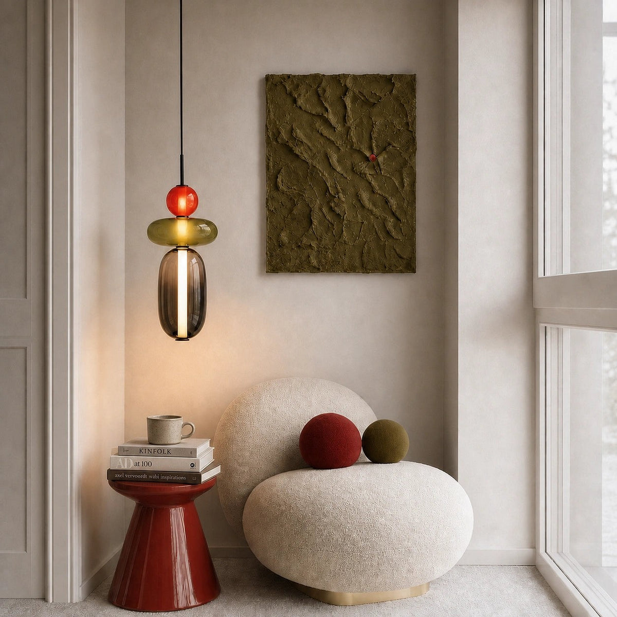 Clérachic pendant hanging in a quiet reading corner above a round boucle chair, its red ball and olive disc softly lit.