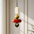 Detail of a Clérachic pendant with an opal capsule, olive ball, wide red disc and a small black ball on a black cord.