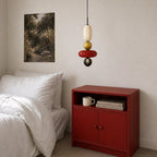 This Clérachic pendant hung beside a bed and a red cabinet, its olive ball and red disc catching the warm light.