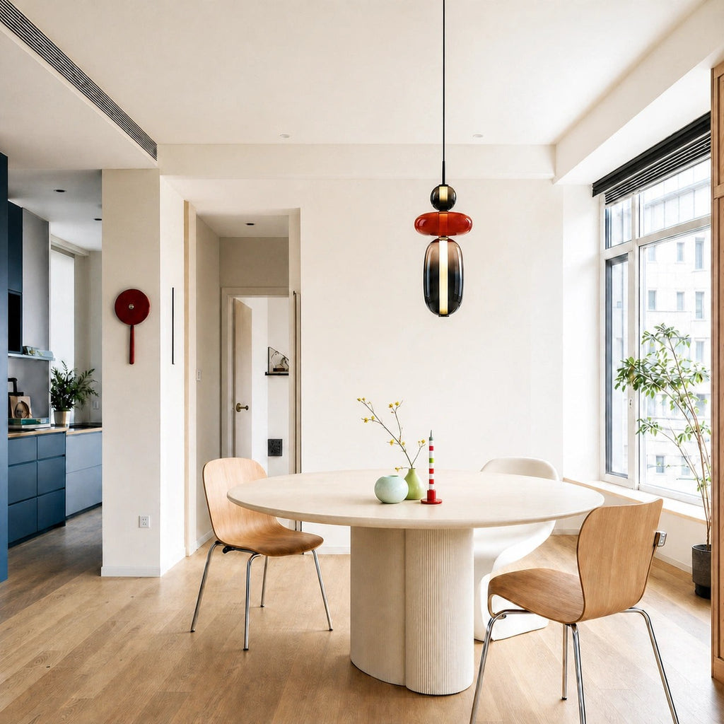 A Clérachic pendant with a black ball, red disc and smoked capsule above a round dining table in a bright open room.