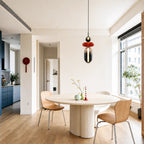 A Clérachic pendant with a black ball, red disc and smoked capsule above a round dining table in a bright open room.
