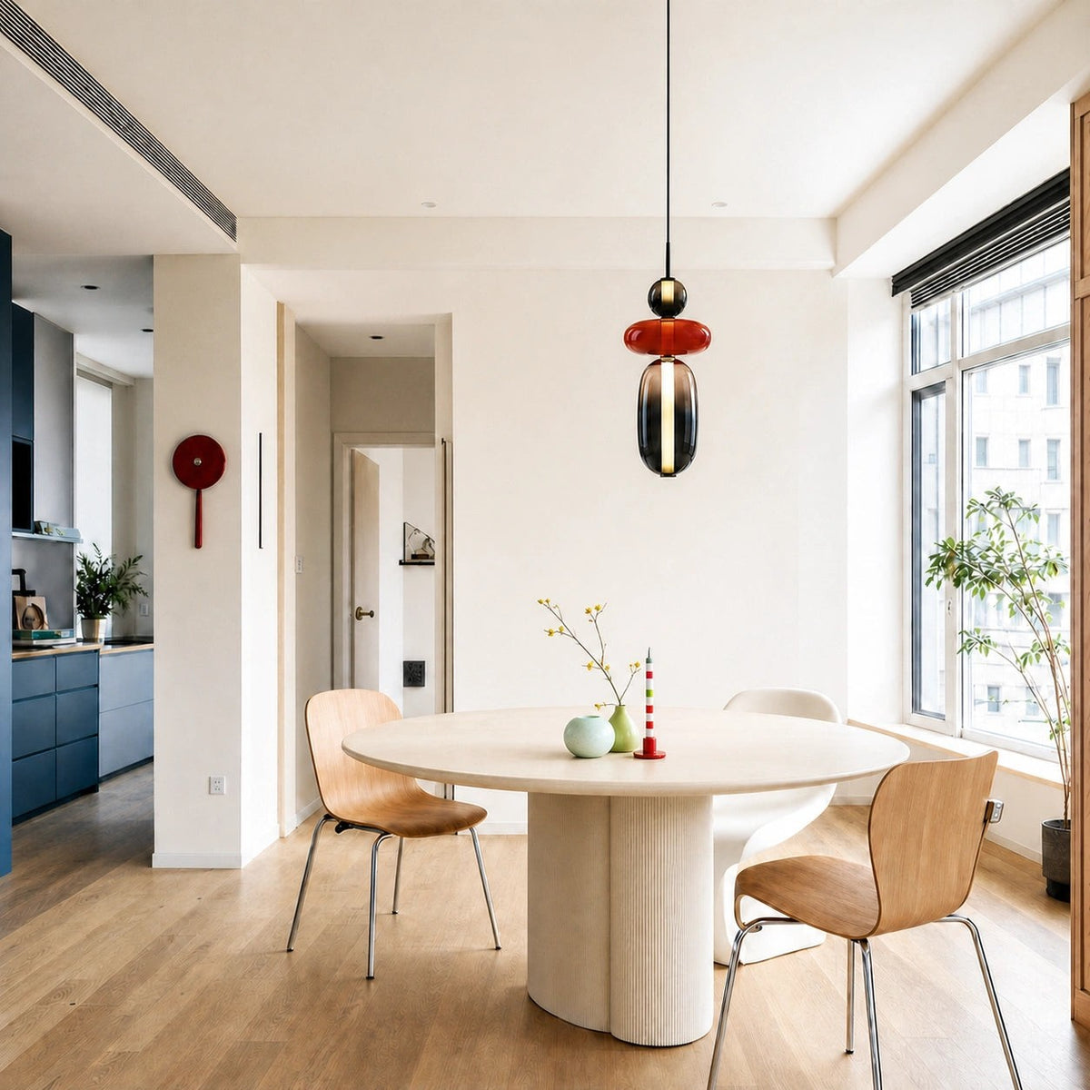 A Clérachic pendant with a black ball, red disc and smoked capsule above a round dining table in a bright open room.