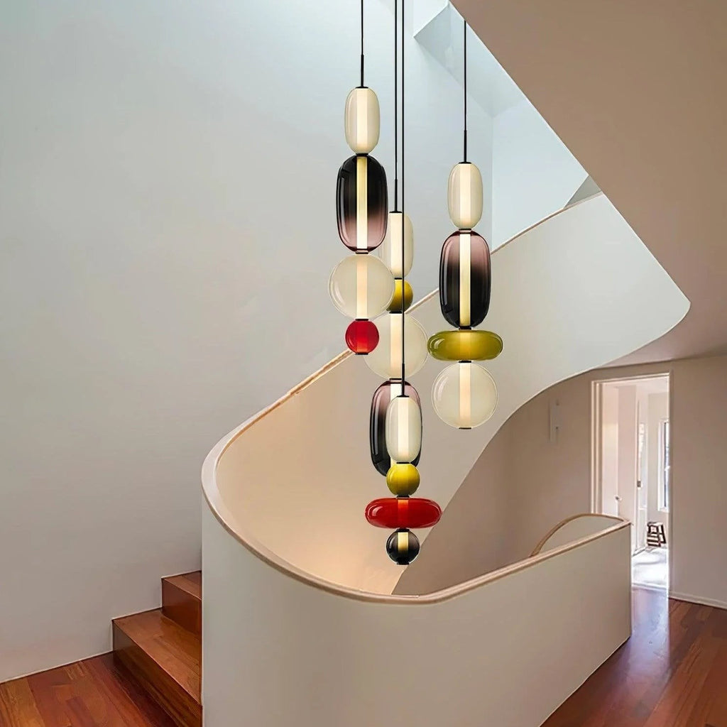 Several Clérachic pendants at different drops in a stairwell, their glass stacks glowing against a curved white wall.