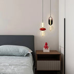 Two Clérachic pendants lit beside a bed with grey linen, one with a red disc and one with a smoked glass capsule.