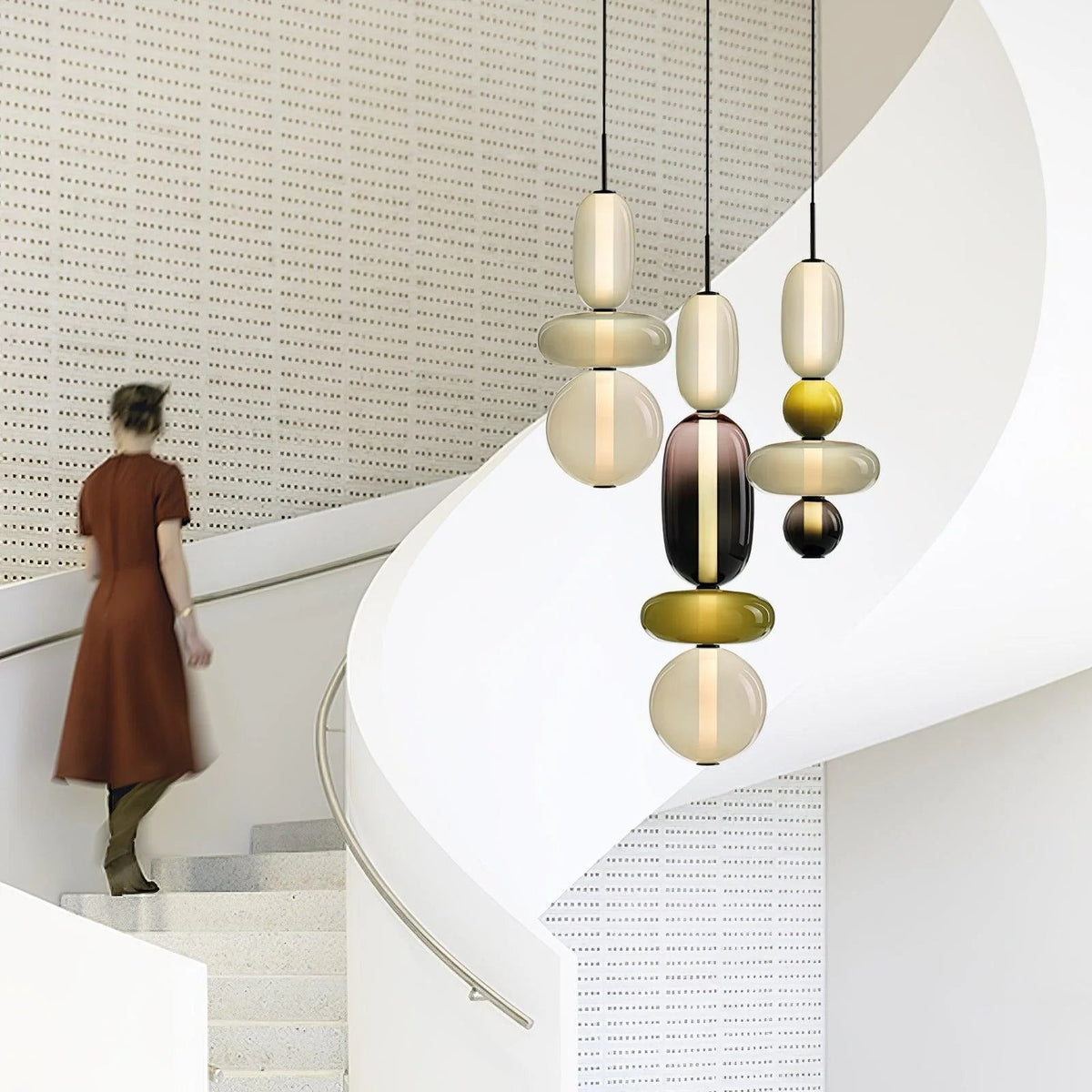 Clérachic pendants hung at staggered heights over a spiral staircase, their olive and smoked glass stacks lit from within.
