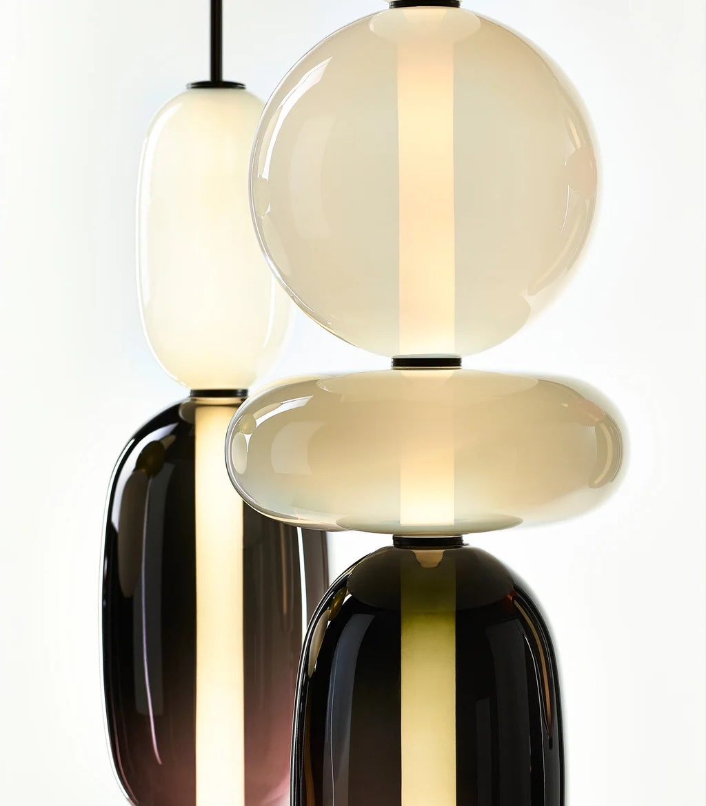 Close view of the hand-blown glass on two Clérachic pendants, an opal sphere and disc over smoked plum glass, each lit through by a slim LED bar.