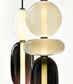 Close view of the hand-blown glass on two Clérachic pendants, an opal sphere and disc over smoked plum glass, each lit through by a slim LED bar.