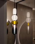 A Clérachic pendant of opal, olive and plum glass lit in a bathroom, its reflection showing in a round backlit mirror.