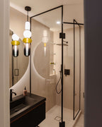 The same Clérachic stacked glass pendant hanging above a black basin beside a glass shower screen.