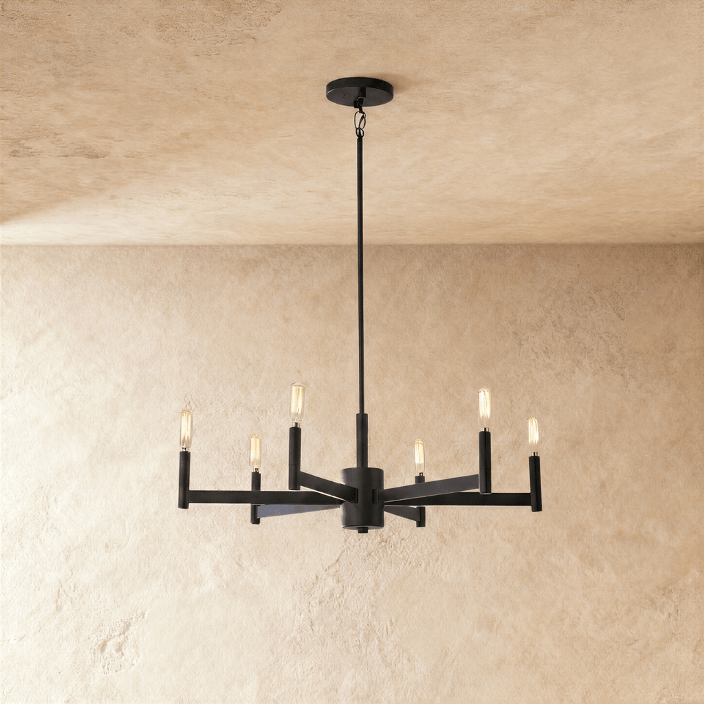 Clérachic six-arm chandelier in matte black with filament-style bulbs on slim candle tubes, hung from a rod against limewash.
