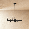 Clérachic six-arm chandelier in matte black with filament-style bulbs on slim candle tubes, hung from a rod against limewash.