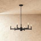 Clérachic six-arm chandelier in matte black with filament-style bulbs on slim candle tubes, hung from a rod against limewash.